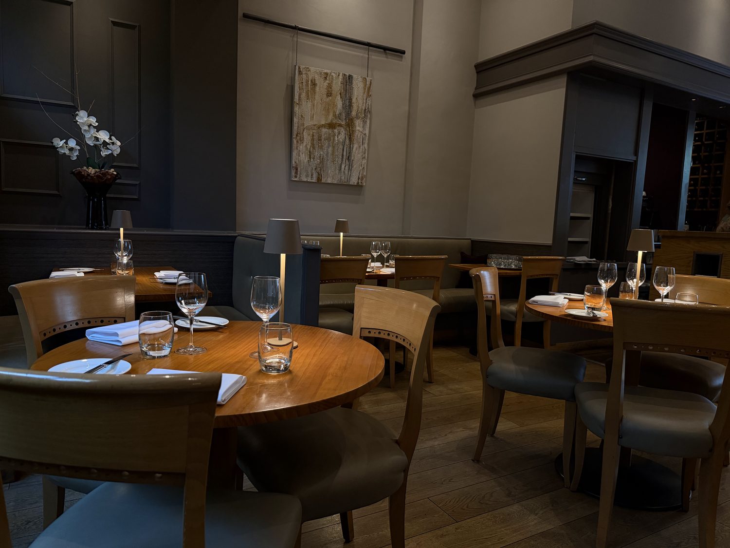 The dining room at Bradley's: wood tables, olive banquette, table lamps and the artwork on the back wall