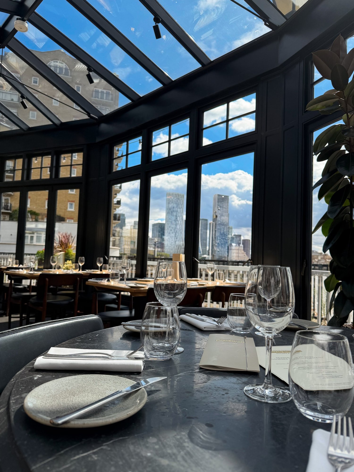 Interior of the conservatory at Bread Street Kitchen Limehouse looking out to the Canary Wharf skyline
