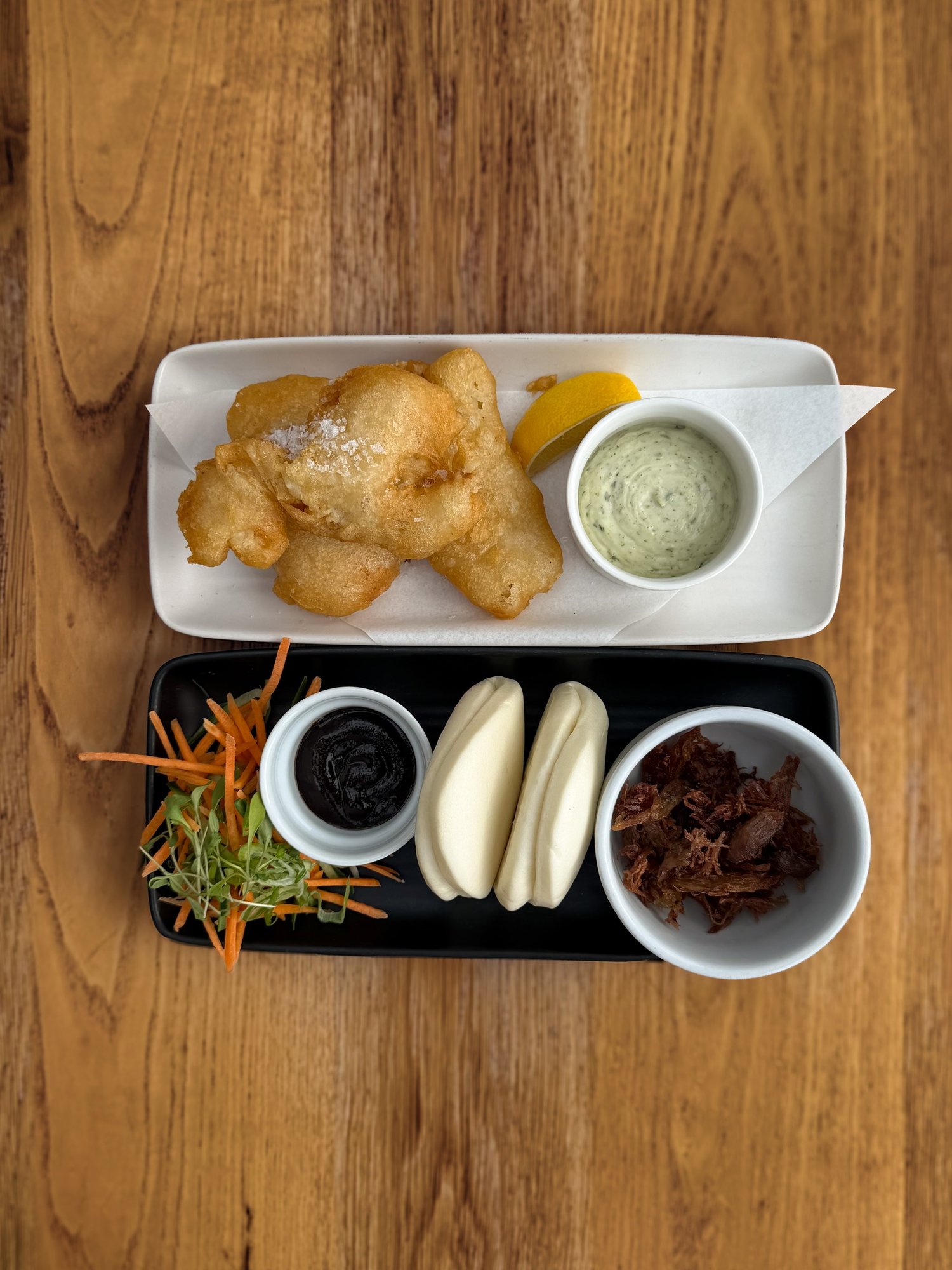 Overhead view of battered cod and haddock bites with tartare sauce and a black board of duck leg bao