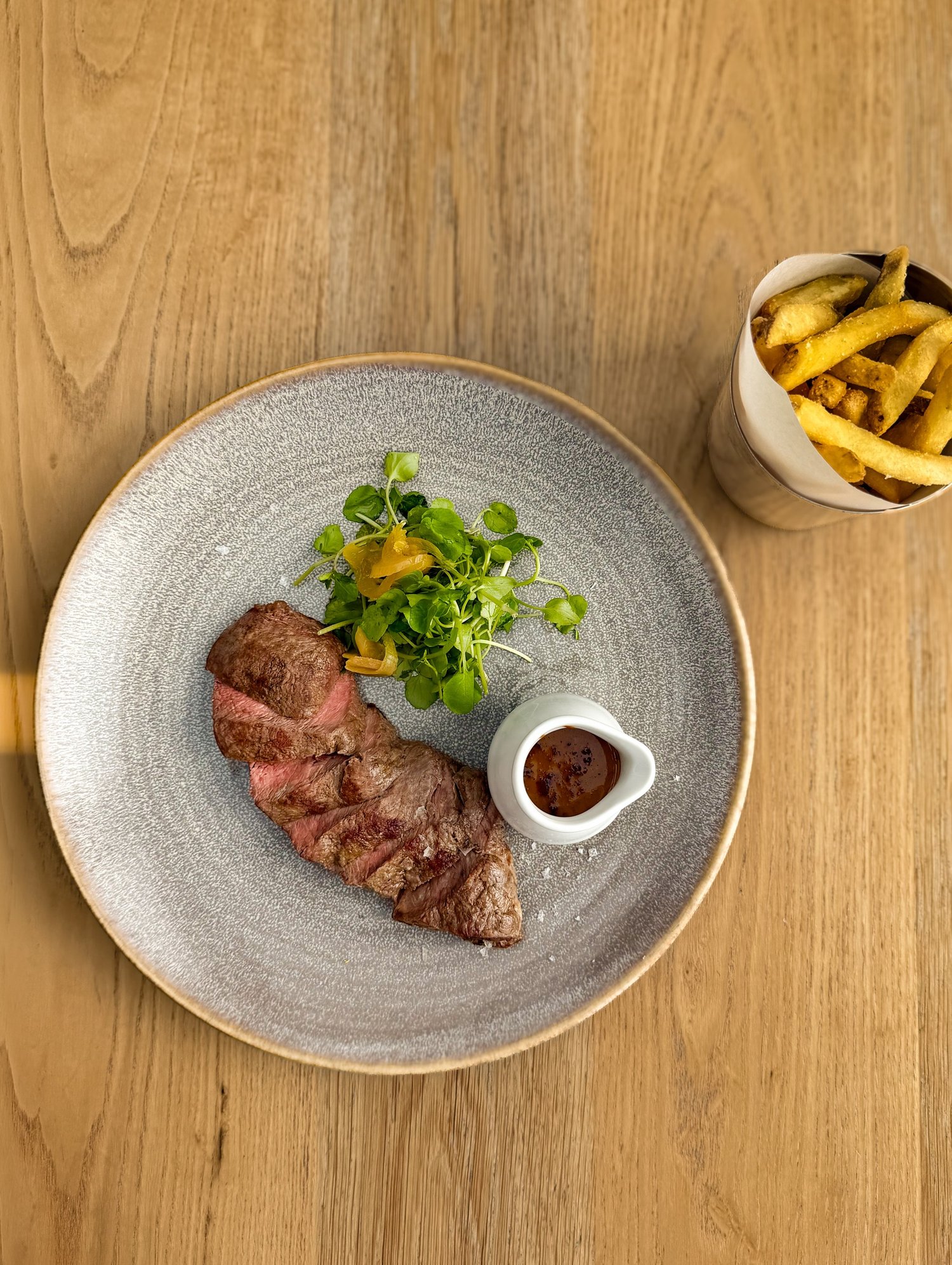 Overhead of grilled flat iron steak with watercress and a jug of peppercorn sauce
