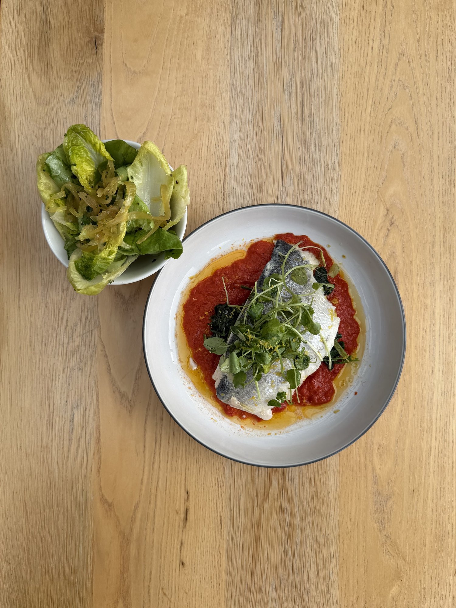 Overhead of steamed sea bream on red pepper tapenade with a side of endive salad