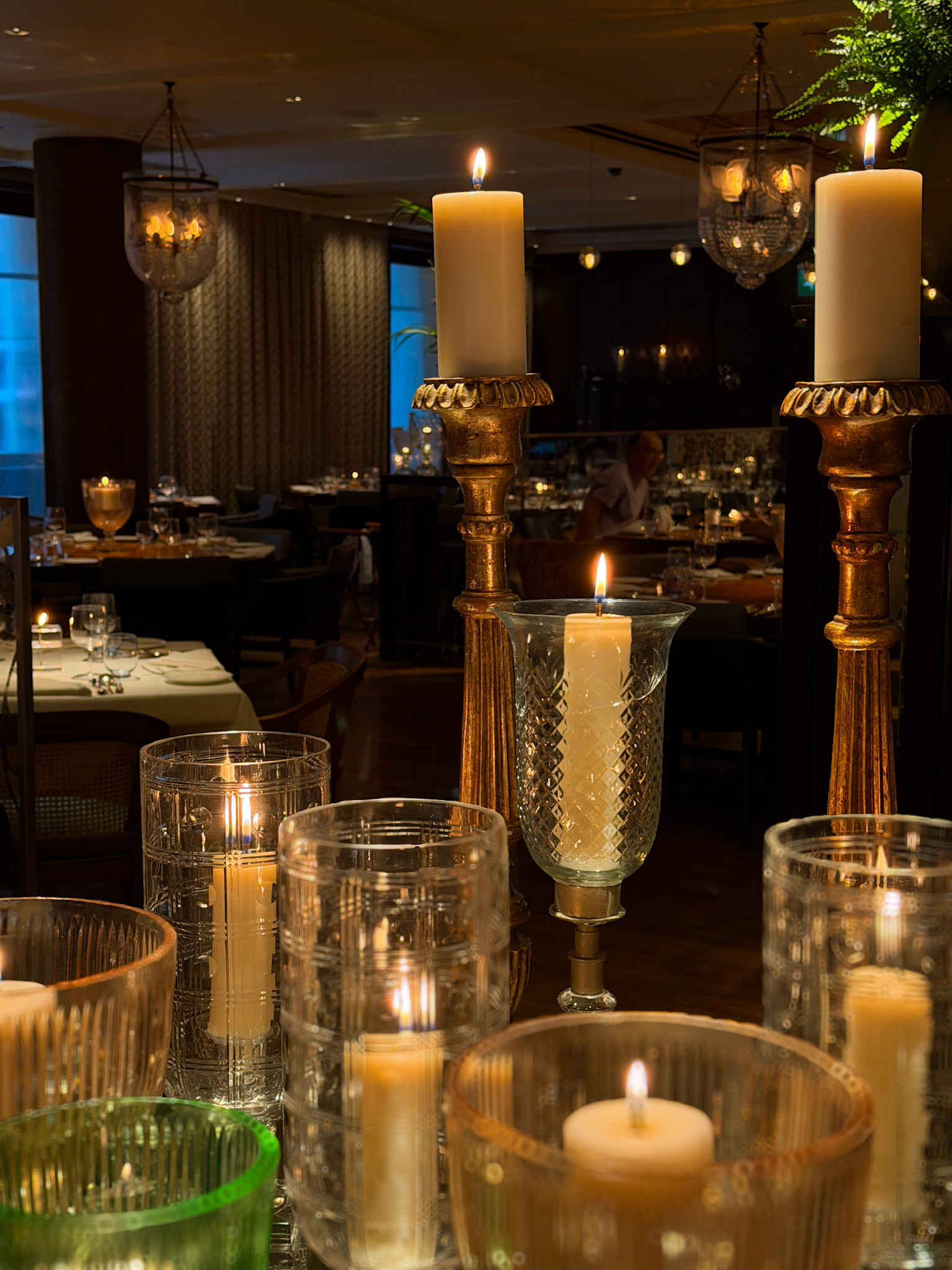Gilded candlesticks and cut crystal hurricanes holding lit candles along the centre of a table