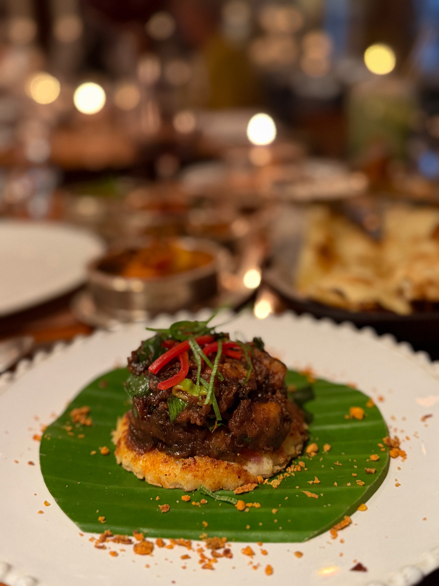 Kerala chicken, dark and glossy with red chilli and coriander, piled on a mini uttapam set on a banana leaf