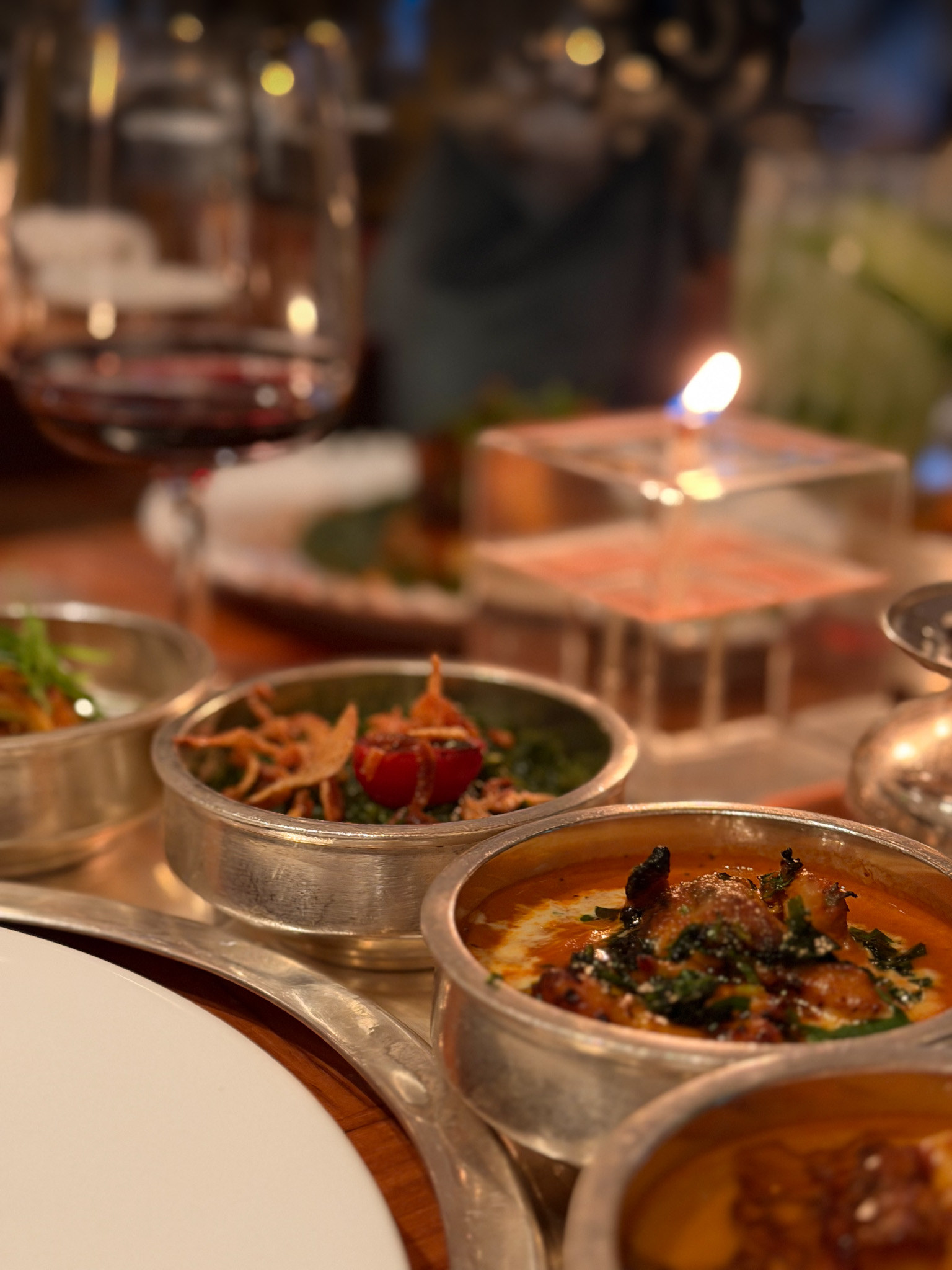 The curved silver tray with spinach saag under crisp fried onion and a halved tomato, and butter chicken alongside