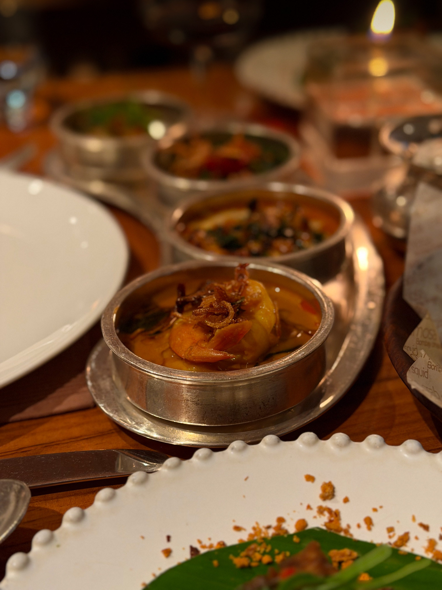 Cochin prawn curry, a whole prawn in a thin golden sauce under crisp fried onion in a small silver bowl