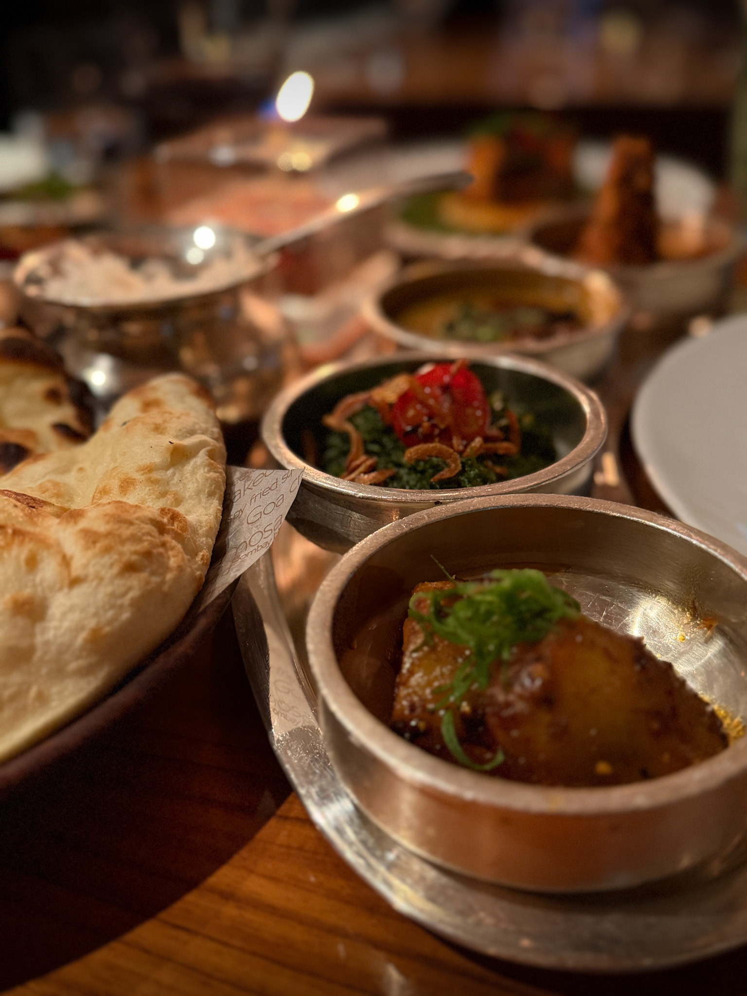 Tandoori sweet potato in a dark sauce under shredded greens, with spinach saag and naan behind