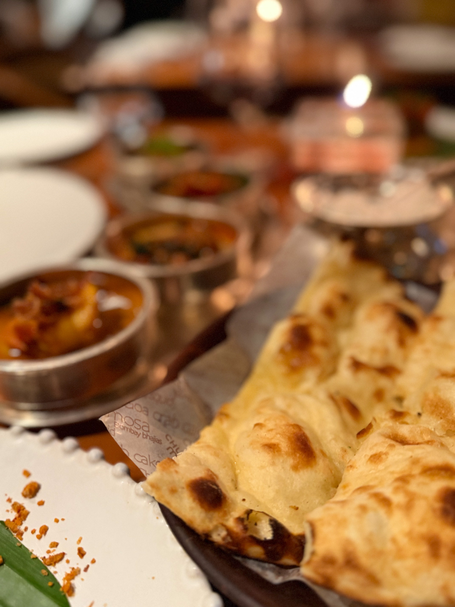 Warm blistered naan folded into a lined basket beside the silver curry bowls
