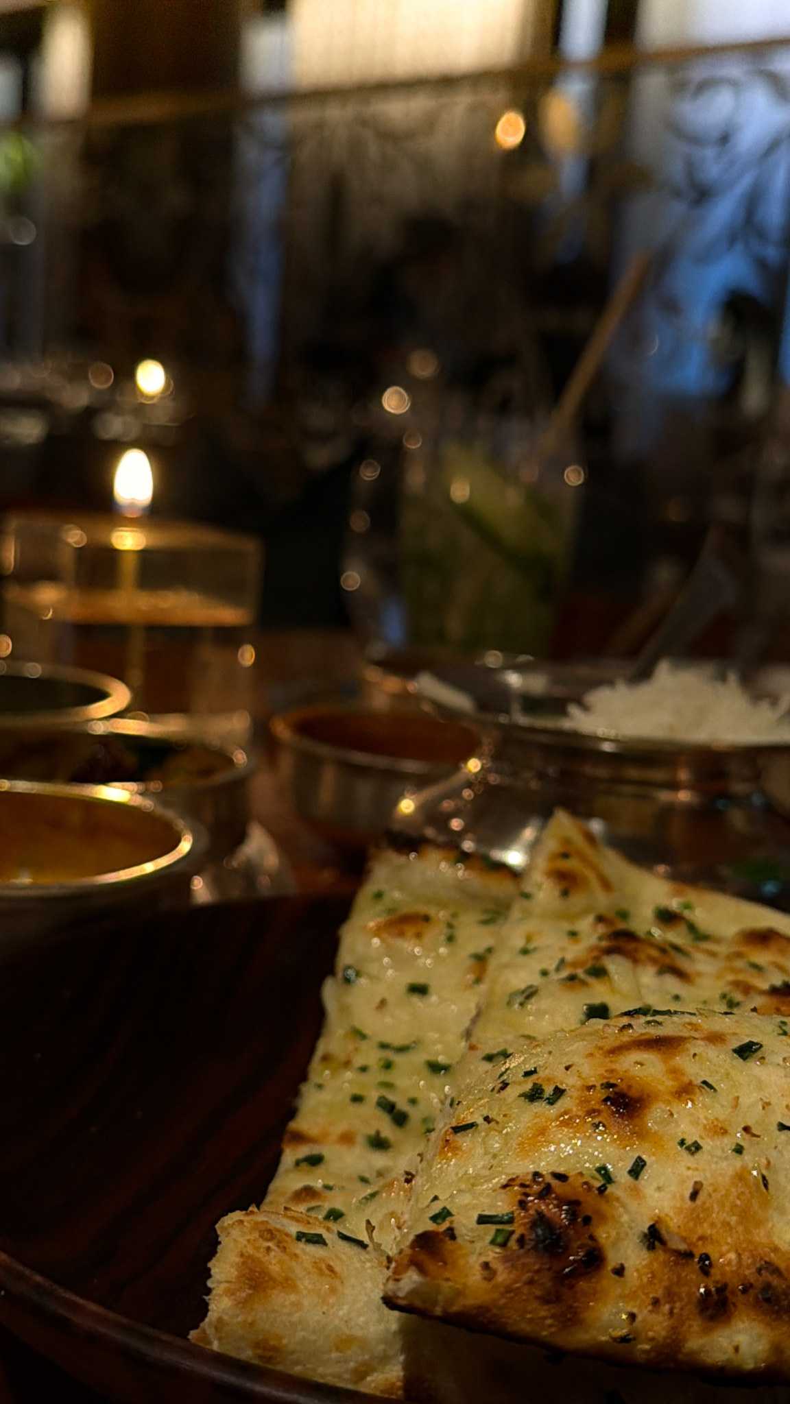A second naan scattered with chopped herbs, with a silver pot of rice behind it