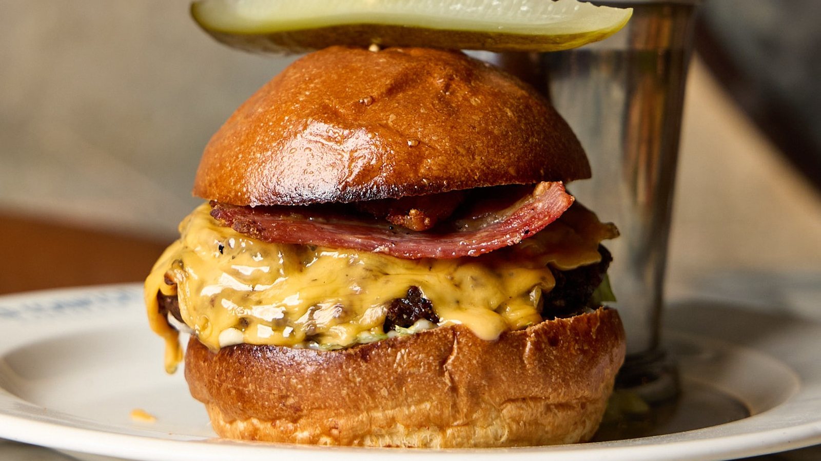 The OCB Burger with melted cheese and a pickle, beside a cup of fries