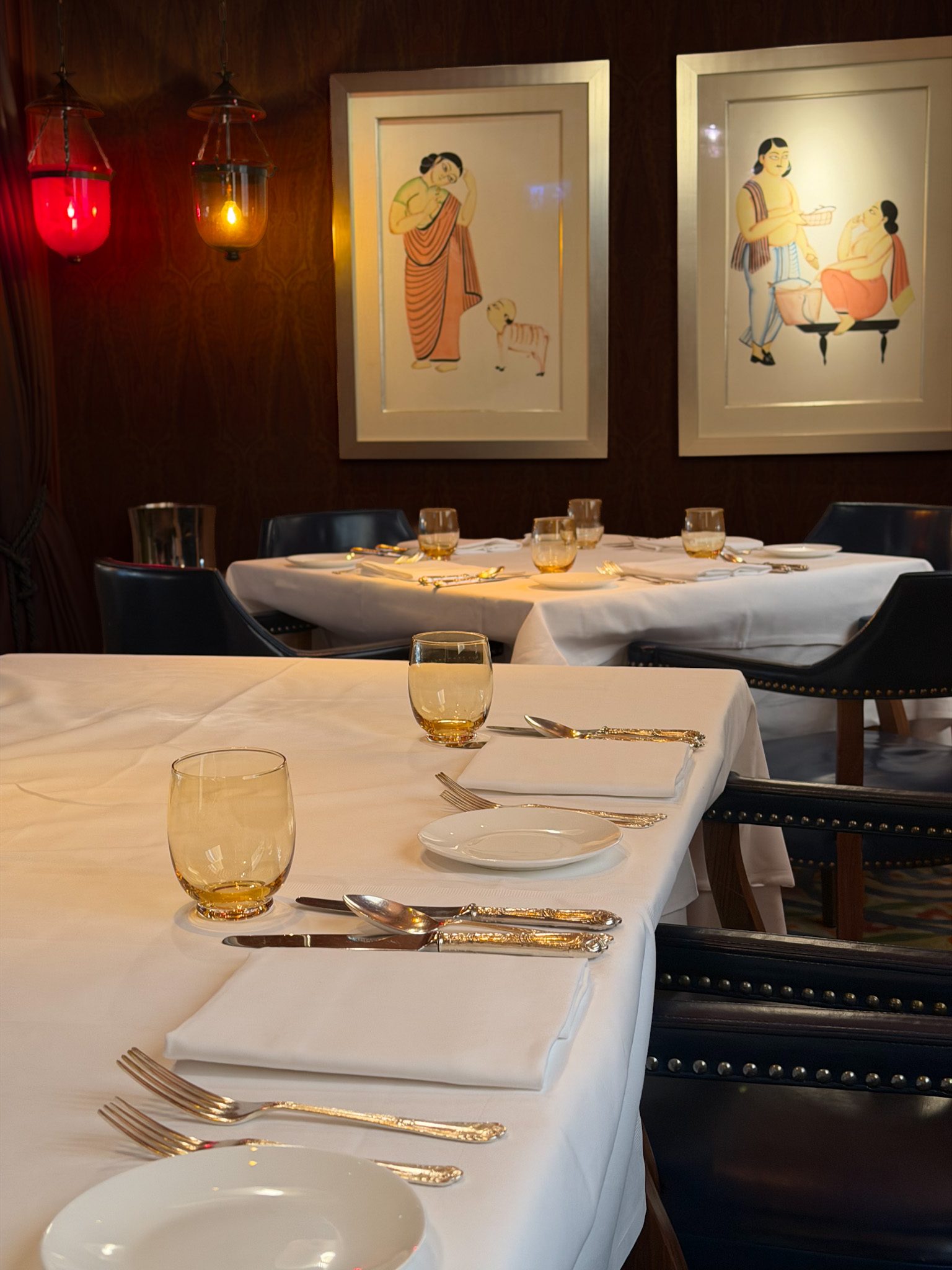 A table laid with white linen and amber glasses beneath framed paintings