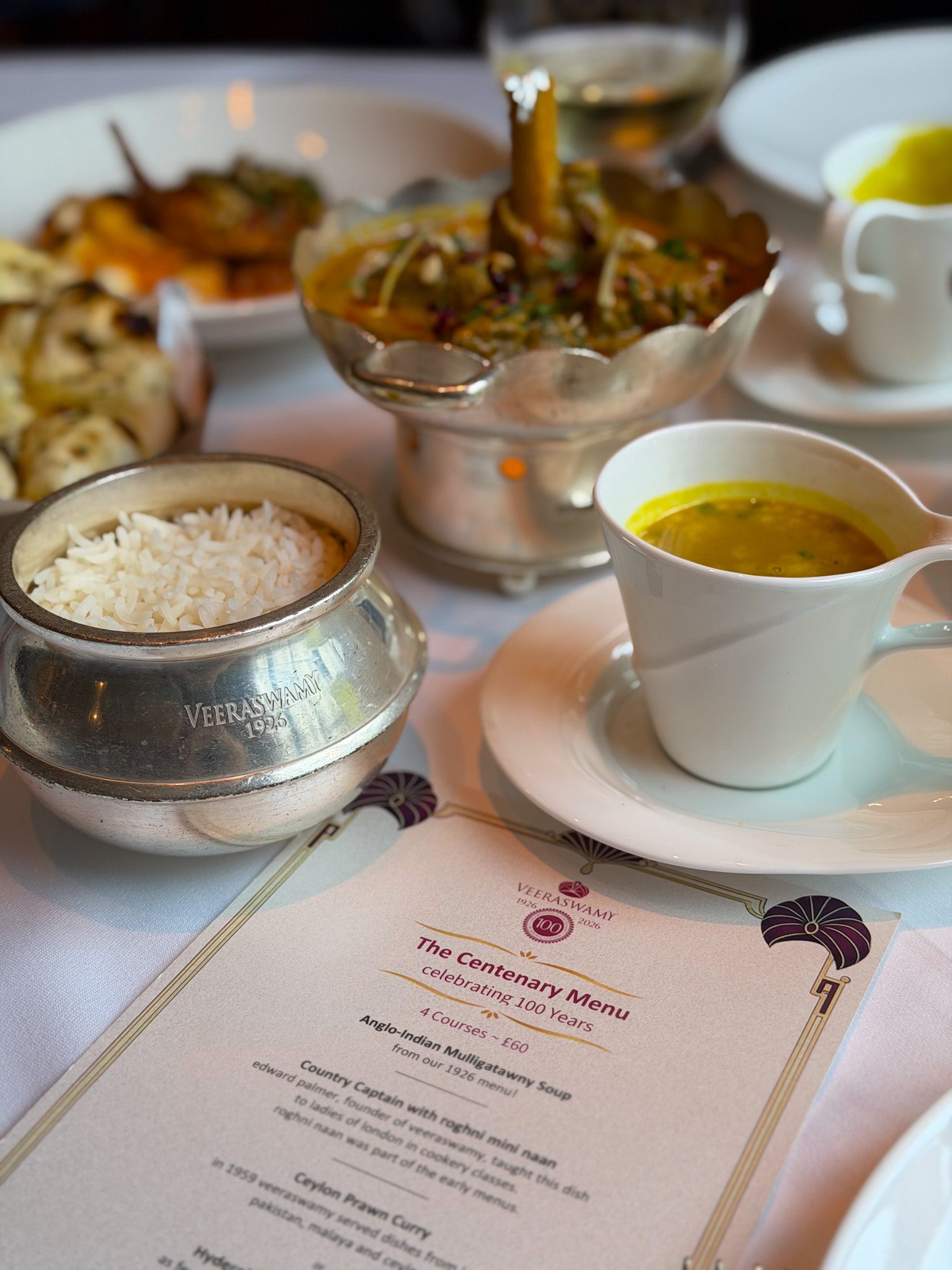 The Centenary Menu card beside a silver pot of basmati rice, a cup of mulligatawny soup and the lamb salan
