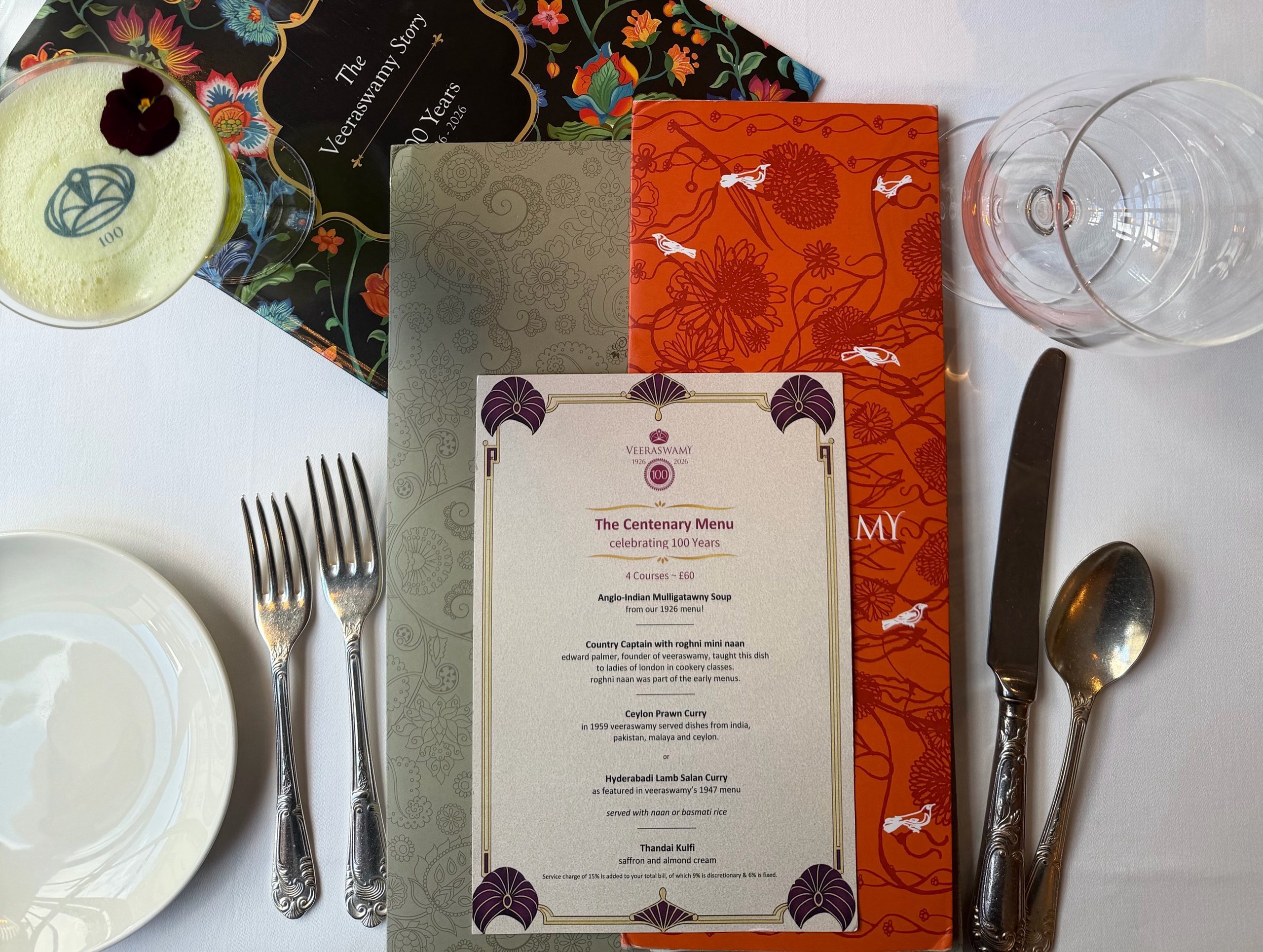 The table laid for the Centenary Menu: the printed menu card, the Veeraswamy Story booklet, cutlery and a centenary cocktail
